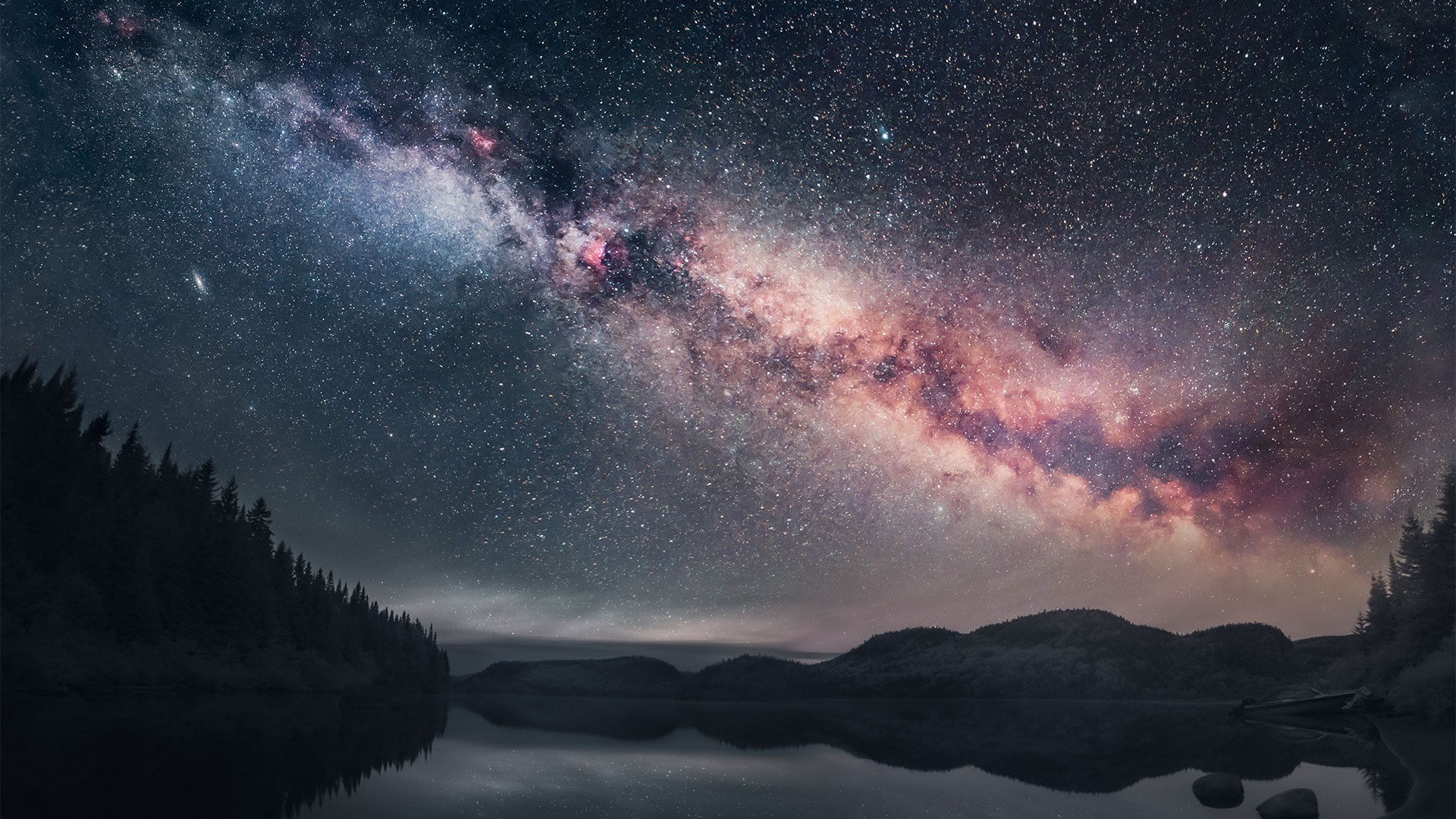 Beautiful image of the milky way illuminating a dark night sky against a forest background and waterway.